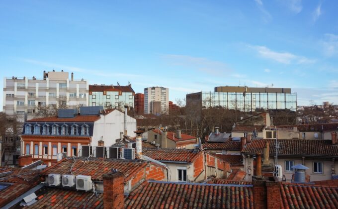 Vue sur les toits en tuiles des vieilles maisons en briques du quartier d'Arnaud Bernard à Toulouse, France, avec en arrière-plan les tours d'habitation et les immeubles de bureaux du quartier Matabiau.