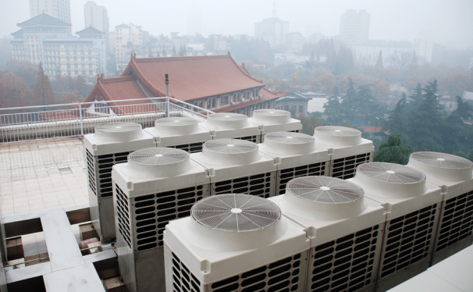 A row of heat pumps on top of a building. In the distance, a skyline of a city is draped in fog. The buildings are a mix of modern architecture and traditional Chinese sloped roofs.